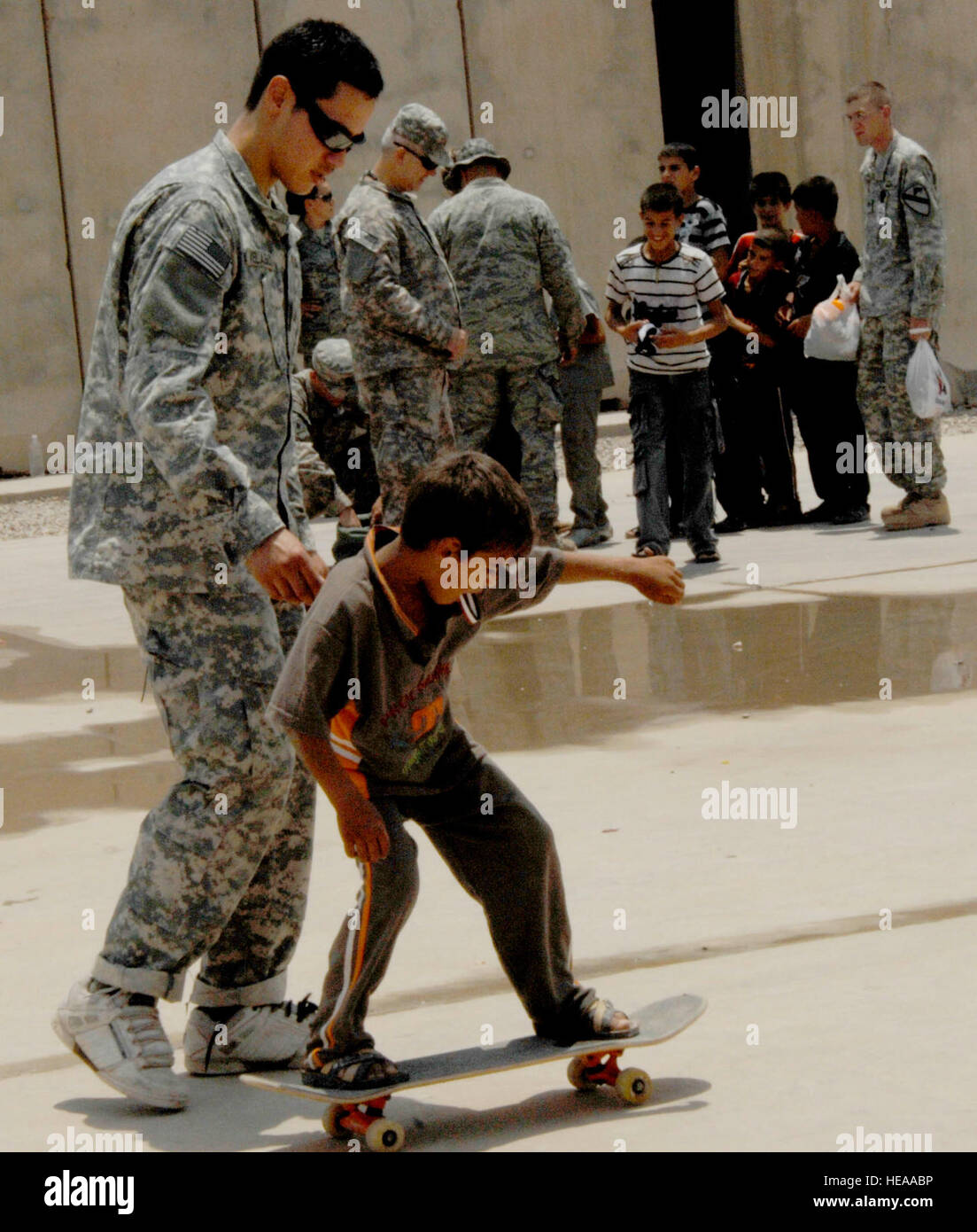 A U.S. Army soldier teaches an Iraqi boy how to skateboard during Iraqi Kids Day held, June 25, 2011, at Joint Base Balad, Iraq. More than 100 volunteers from across JBB volunteered to spend a few hours with the children and learn about their culture while the children learned a little about the military and American culture. Stock Photo