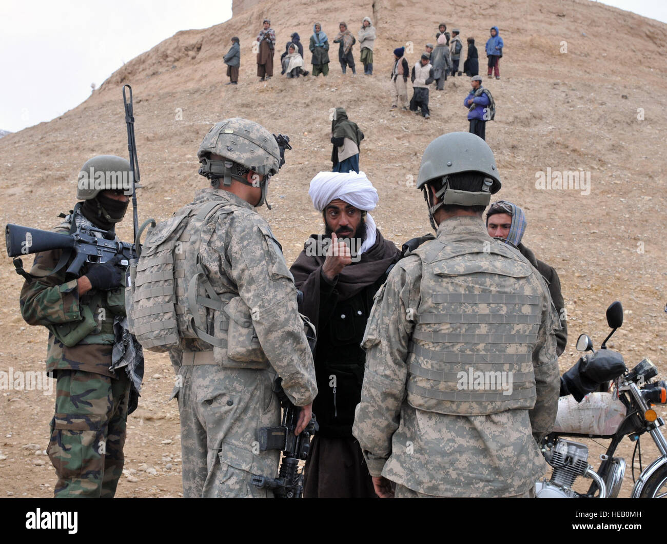 A local Afghan man from Nawbor Village, Bala Murghab district, Baghdis province, Afghanistan, talks through an interpreter (right) to (left) U.S. Army Staff Sgt. Nicholas Lewis, a scout with White Platoon, Bulldog Troop, 7th Squadron, 10th Cavalry Regiment, 1st Brigade, 4th Infantry Division, at Fort Carson, Colo., Jan. 16, 2011. The Afghan thanked the Afghan National Army and U.S. Army scouts for ridding his village of insurgents and bringing a better life to the Nawbor children, who gathered on the hill. Stock Photo