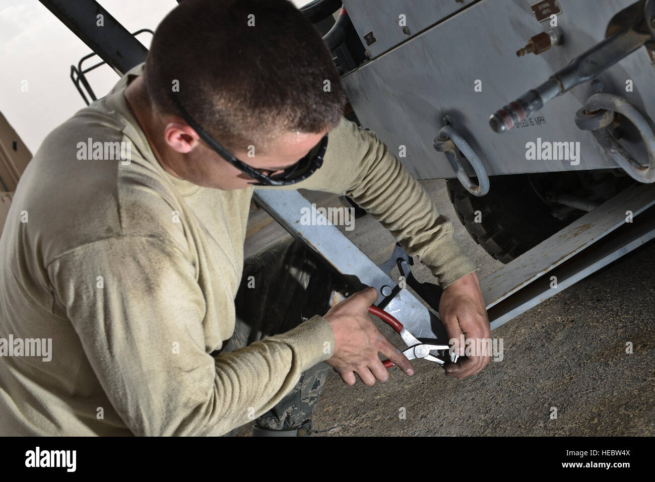 Senior Airman Daniel Suarez, 379th Expeditionary Maintenance Squadron, fastens a linchpin on a tow bar for an aircraft air conditioning unit May 7, 2015, at Al Udeid Air Base, Qatar. Even through wet-bulb globe temperature index of black flag conditions, airmen remain resilient and practice safe measures to ensure their wingman and themselves are protected from the extreme sun and heat wearing eye protection and sometimes long sleeves. (U.S. Air Force photo by Staff Sgt. Alexandre Montes) Stock Photo