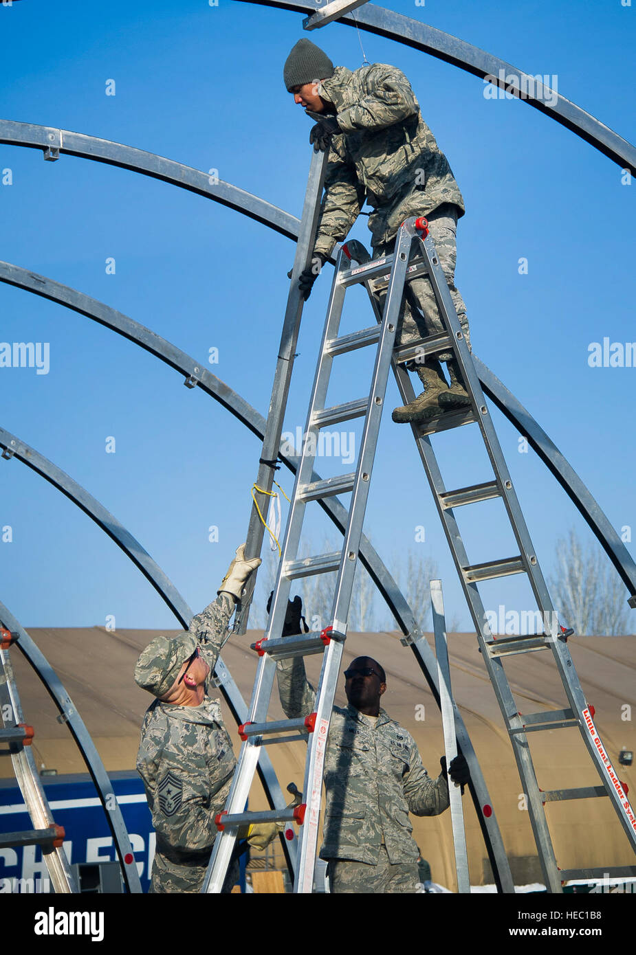 U.S. Air Force Senior Airman Julian Andes, top, a structures technician with the 376th Expeditionary Civil Engineer Squadron, hands a support beam to Chief Master Sgt. Gregory Warren, a command chief with the 376th Air Expeditionary Wing, at the Transit Center at Manas, Kyrgyzstan, March 4, 2014. Airmen with the 376th Expeditionary Civil Engineer Squadron completed dismantling tents in preparation for returning the leased land to Kyrgyz leaseholders. U.S. and international forces in 2013 began the process of drawing down assets in Afghanistan ahead of the eventual transition to handing over Af Stock Photo