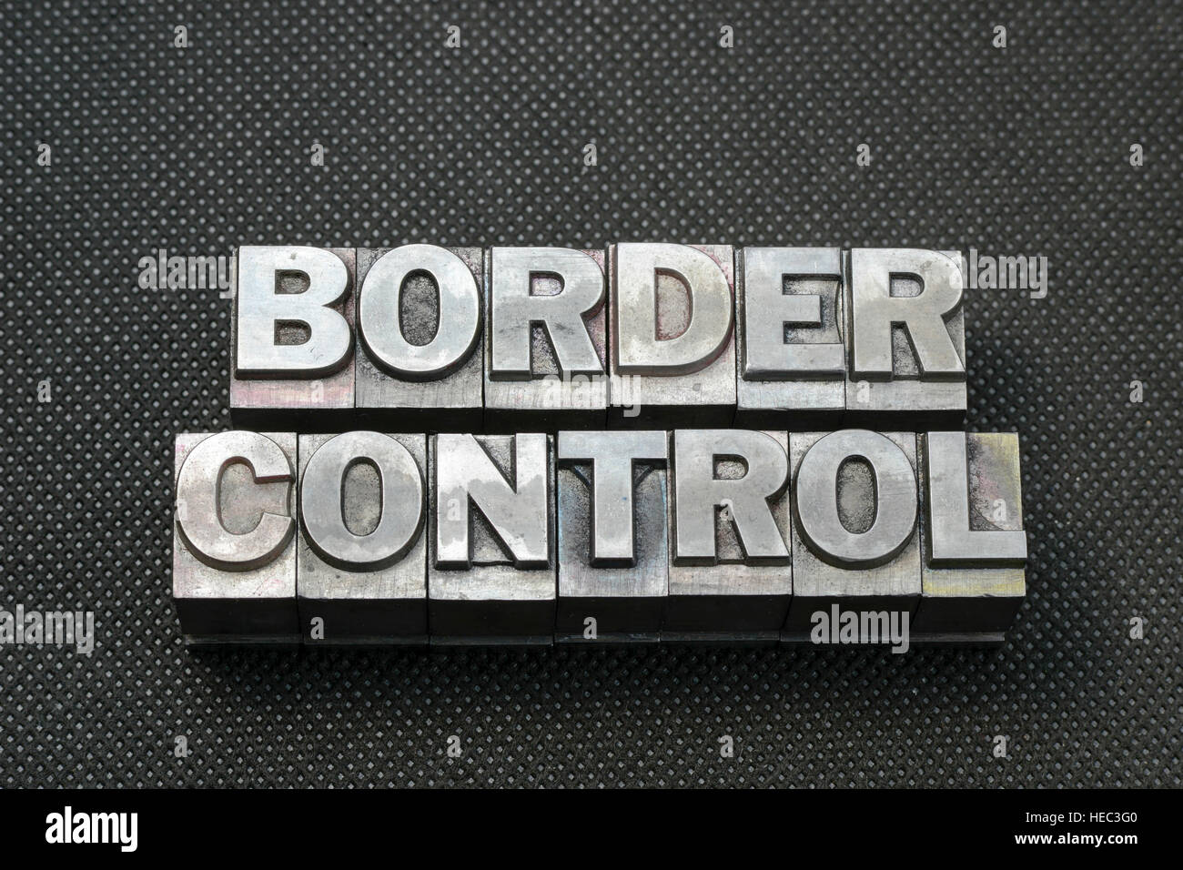 border control phrase made from metallic letterpress blocks on black perforated surface Stock Photo