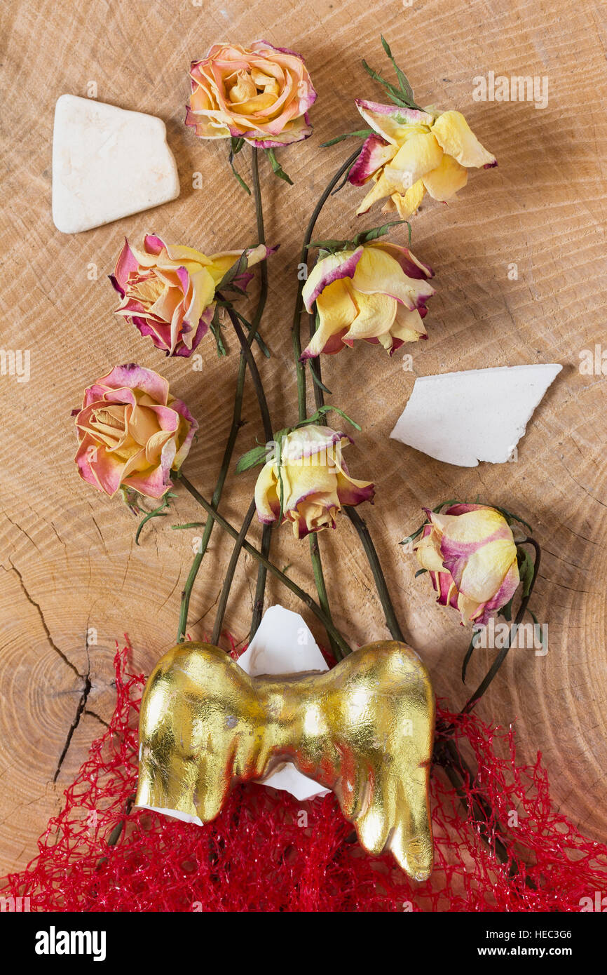 Withered faded sad roses, red net and golden broken angel wings on wooden background as studio close up, symbolic fantasy image Stock Photo