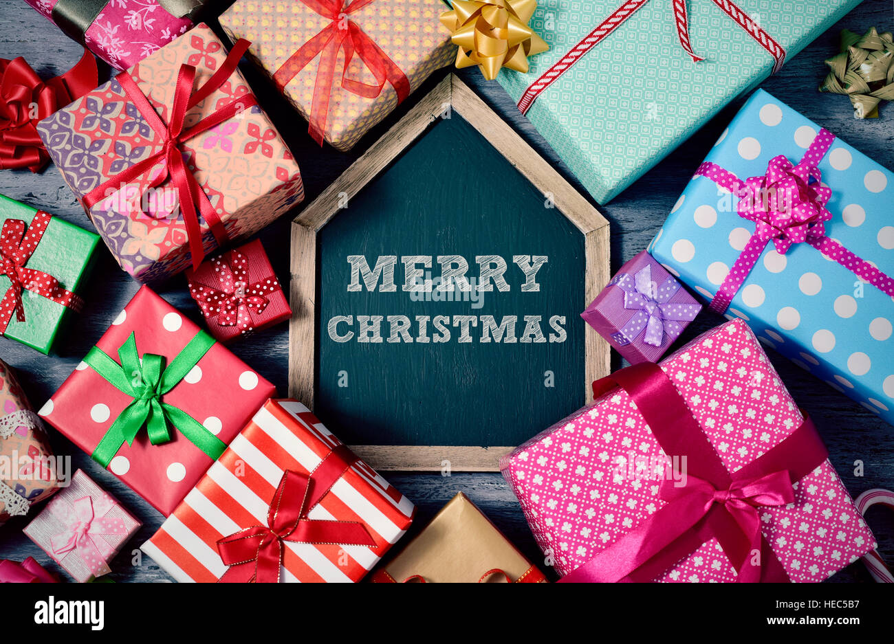 high-angle shot of a pile of gifts wrapped in nice papers and tied with ribbons, and a house-shaped chalkboard with the text merry christmas written i Stock Photo