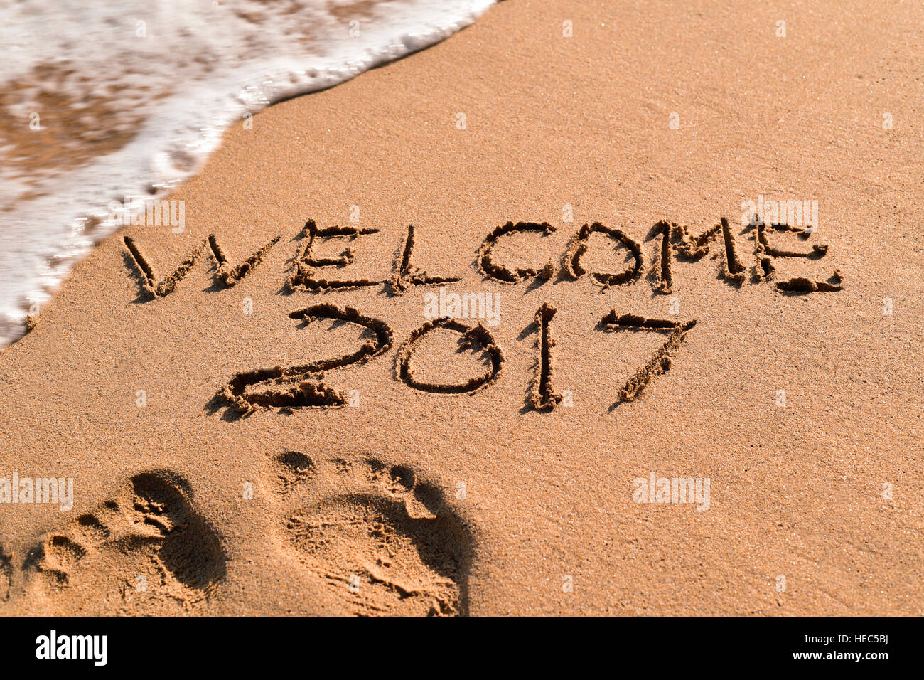 some foot prints and the text welcome 2017 written in the sand of a beach Stock Photo