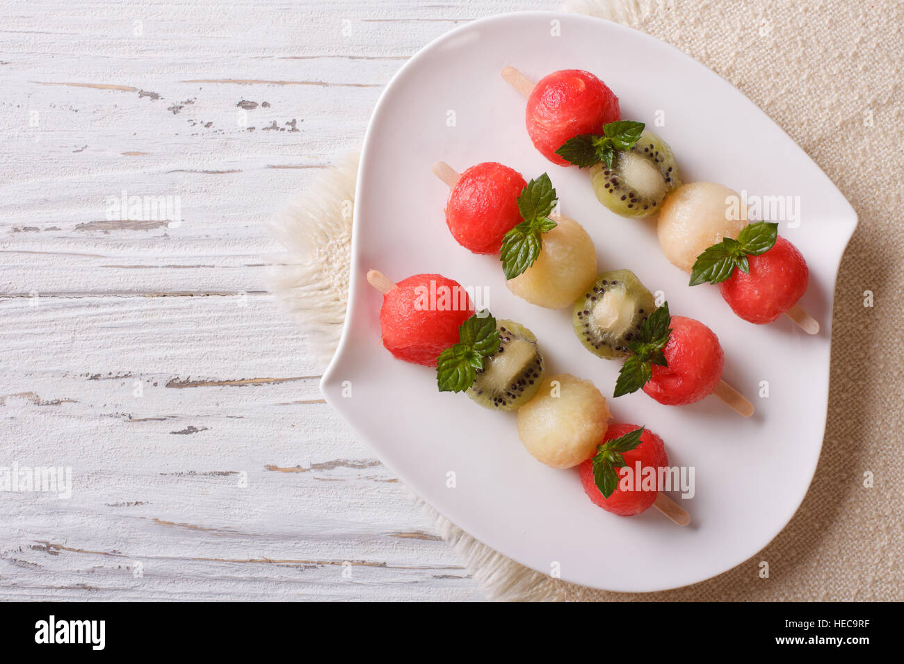 Fruit skewers with balls of watermelon, kiwi and melon on a plate. Horizontal top view Stock Photo