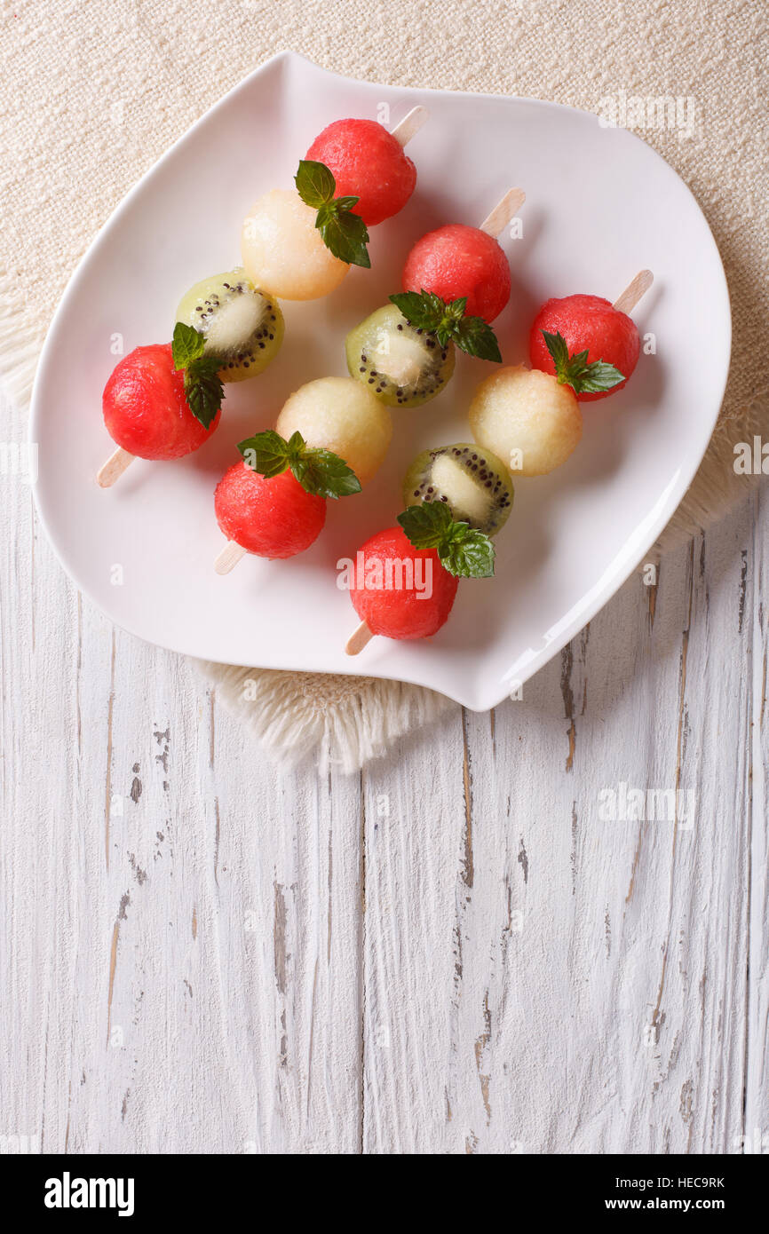 Fruit skewers with balls of watermelon, kiwi and melon on a plate. vertical top view Stock Photo