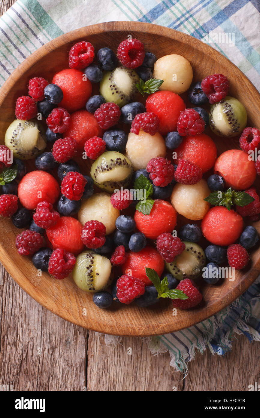 salad of blueberries, raspberries, melon and watermelon in a wooden bowl closeup. vertical top view Stock Photo