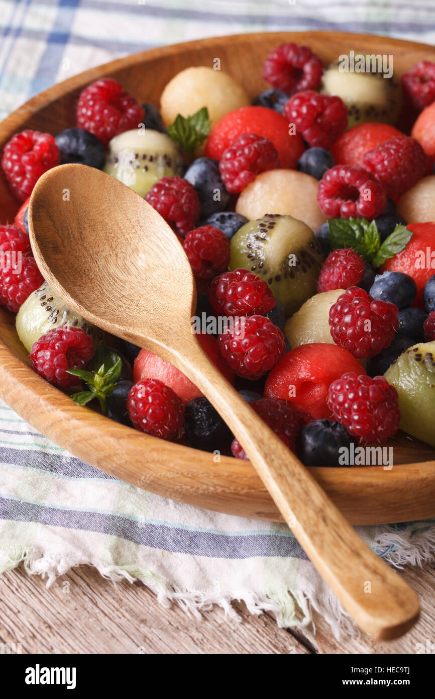 fruit salad of blueberries, watermelon, raspberry, melon and kiwi in wooden bowl closeup. Vertical Stock Photo