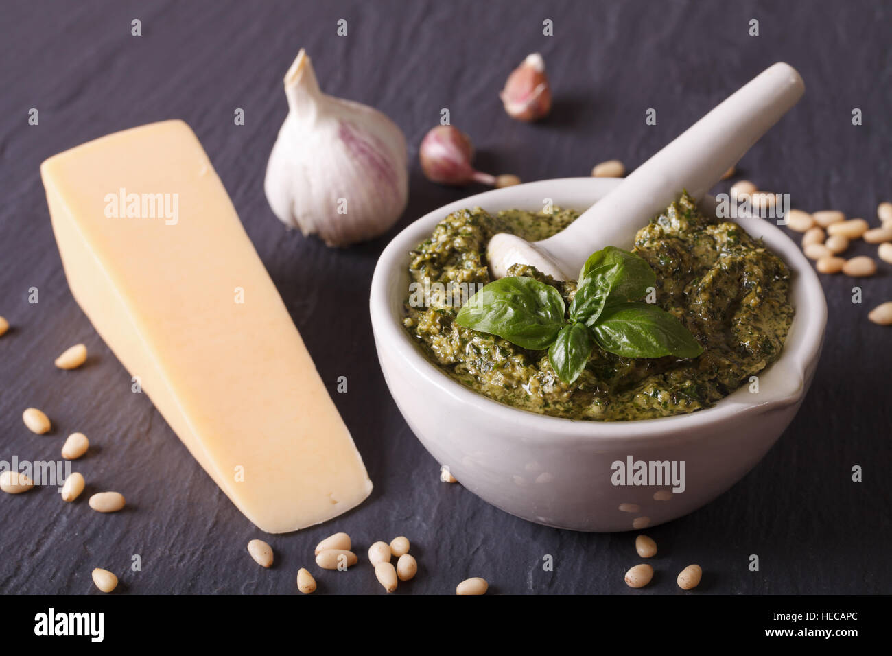Italian green pesto sauce in a mortar and ingredients close-up on the table. Horizontal Stock Photo