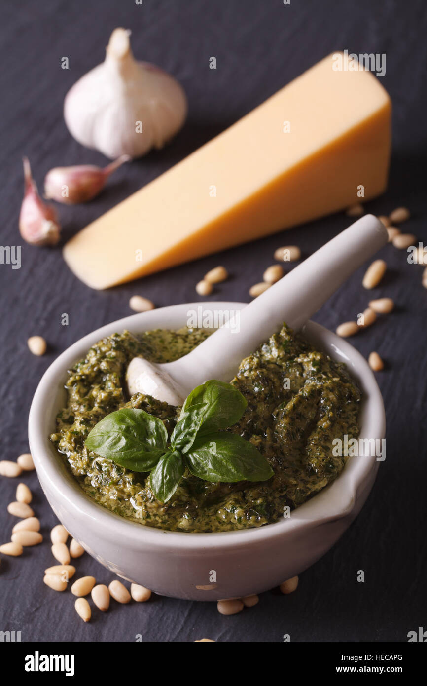Italian green pesto sauce in a mortar and ingredients close-up on the table. vertical Stock Photo