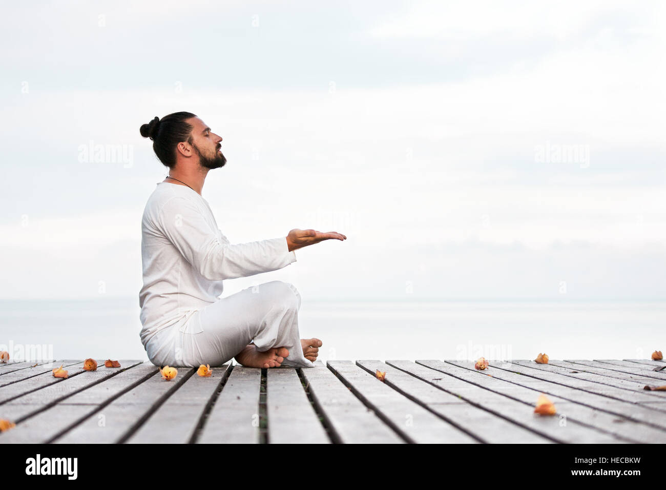 Caucasian man in white clothes meditating yoga on wooden pier platform Stock Photo