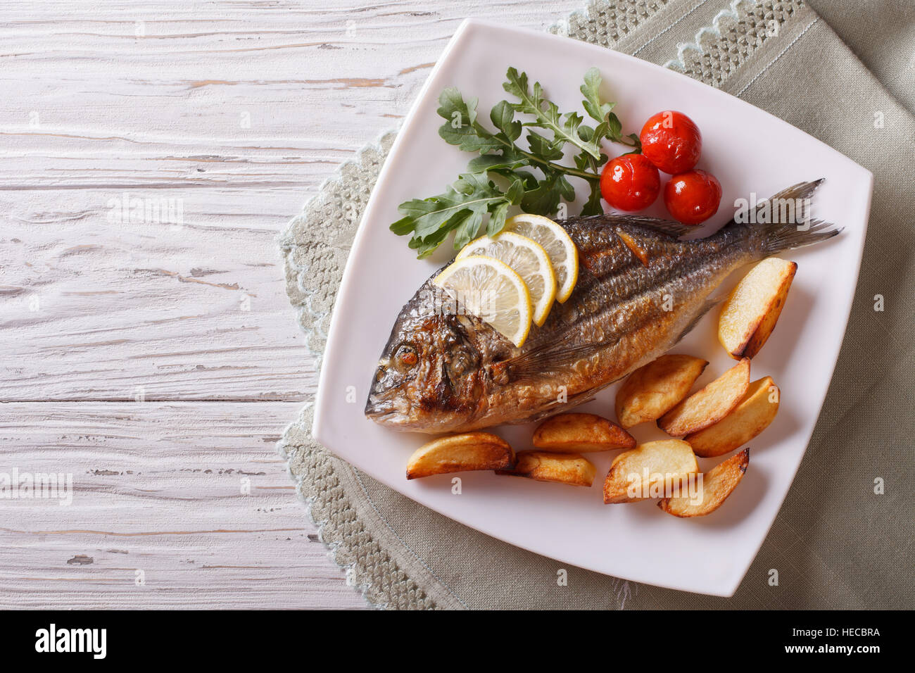 Grilled dorado fish with fried potatoes, lemon and tomato close-up on a plate. horizontal top view Stock Photo