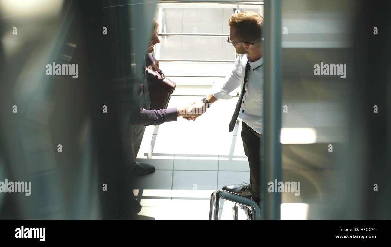 Full length side view of businessmen shaking hands in office building ...
