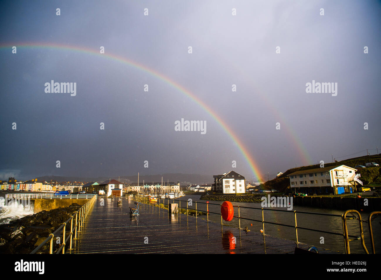 Aberystwyth, Wales, UK. 21 December 2016. UK Weather. On the shortest day of the year, the Winter Solstice, a change in the weather brings showers of rain and gusty winds combined with the high tide to drive huge waves to batter the seafront and harbor wall at Aberystwyth on the Cardigan Bay coast of the Irish Sea in West Wales UK In a brief respite from the rain, a rainbow forms over the town and stormy seas photo © Keith Morris/Alamy Live News Stock Photo