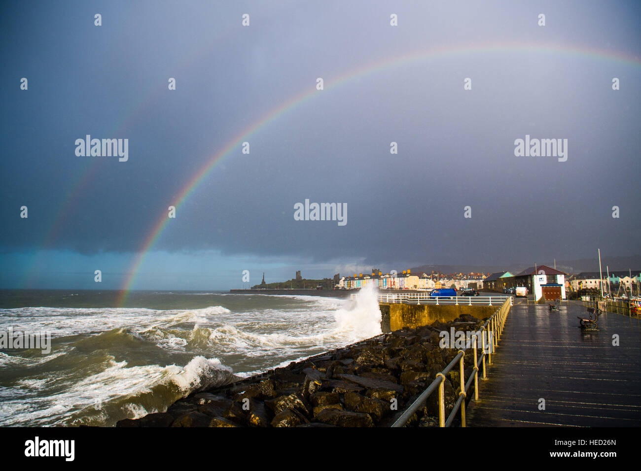 Aberystwyth, Wales, UK. 21 December 2016. UK Weather. On the shortest day of the year, the Winter Solstice, a change in the weather brings showers of rain and gusty winds combined with the high tide to drive huge waves to batter the seafront and harbor wall at Aberystwyth on the Cardigan Bay coast of the Irish Sea in West Wales UK In a brief respite from the rain, a rainbow forms over the town and stormy seas photo © Keith Morris/Alamy Live News Stock Photo