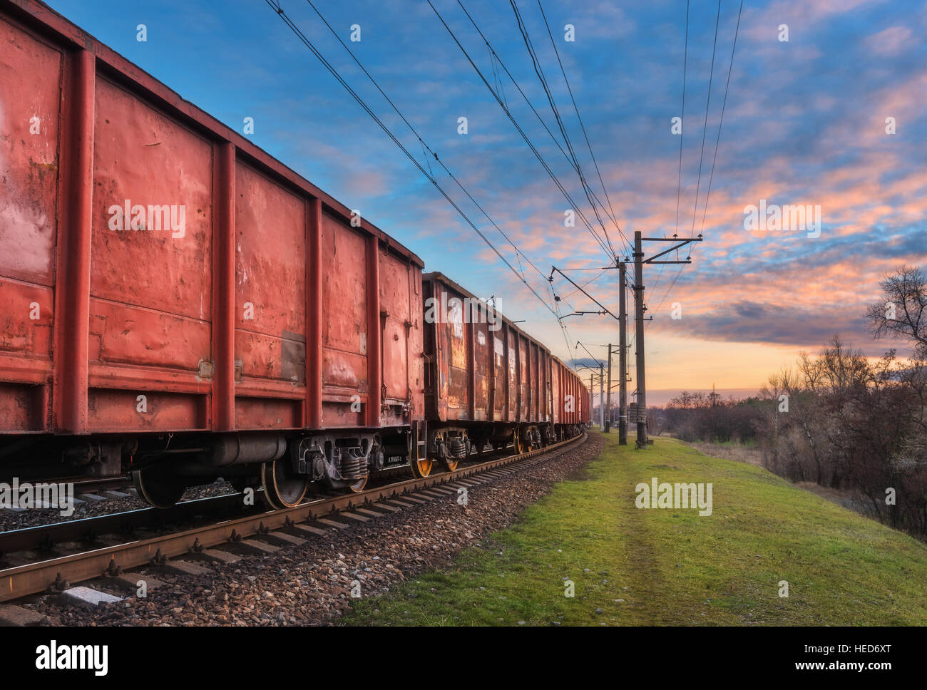 Railway station with cargo wagons and train against blue sky with clouds at sunset. Colorful industrial landscape. Railroad Stock Photo