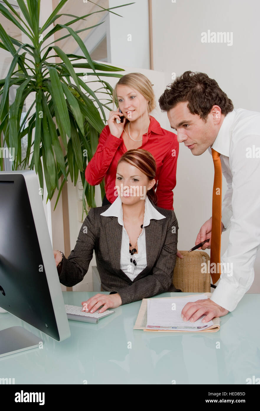 Three young businesspeople gathered around a computer at the office ...