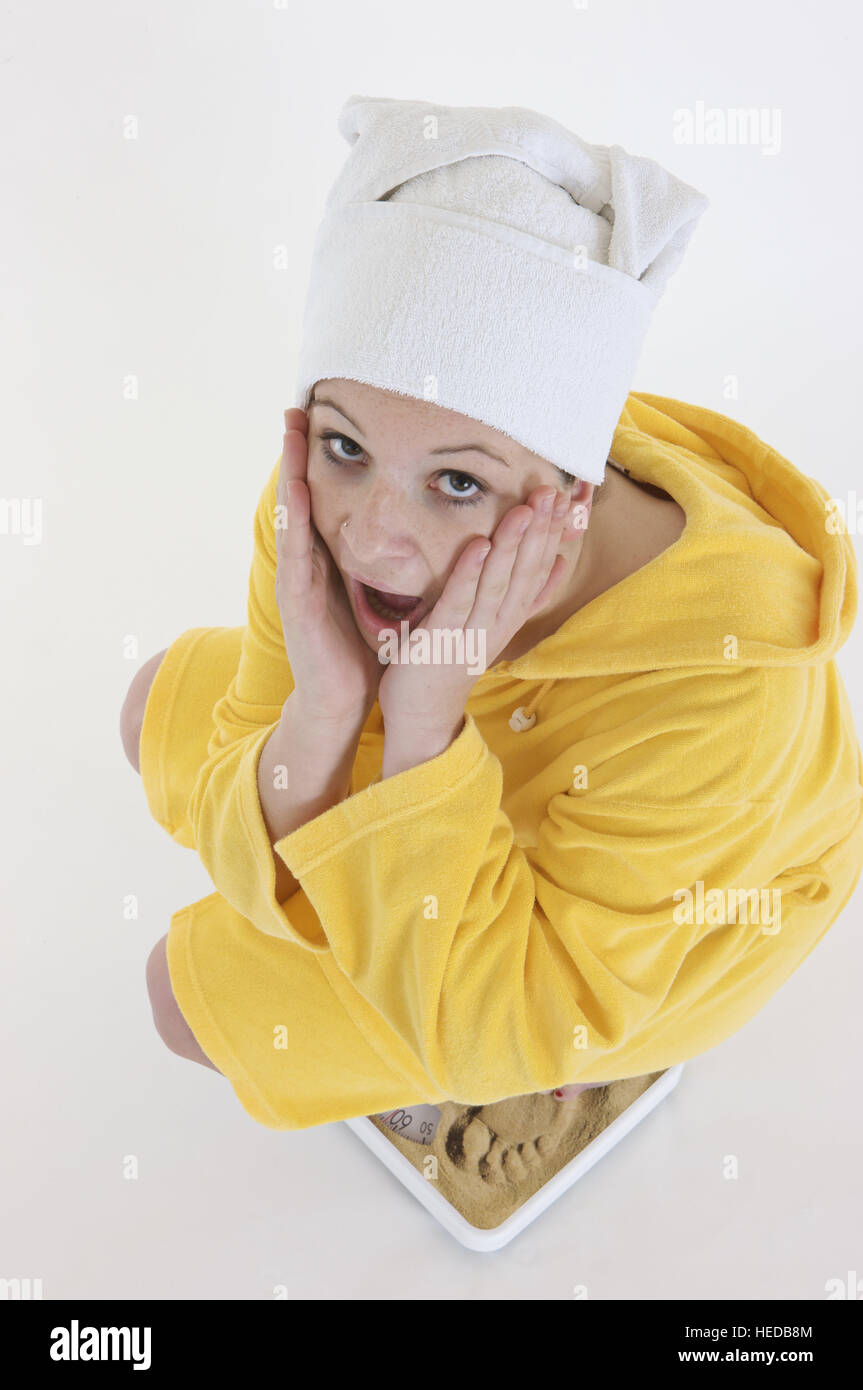 Woman looking shocked as she weighs herself on the weighing scale Stock Photo