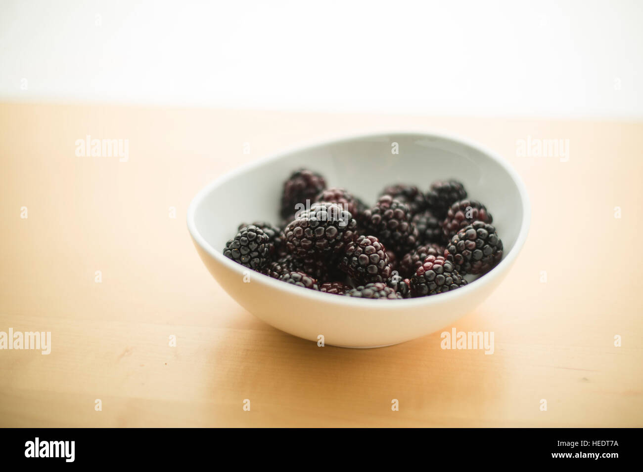 A white ceramic bowl piled with fresh organic blackberries Stock Photo