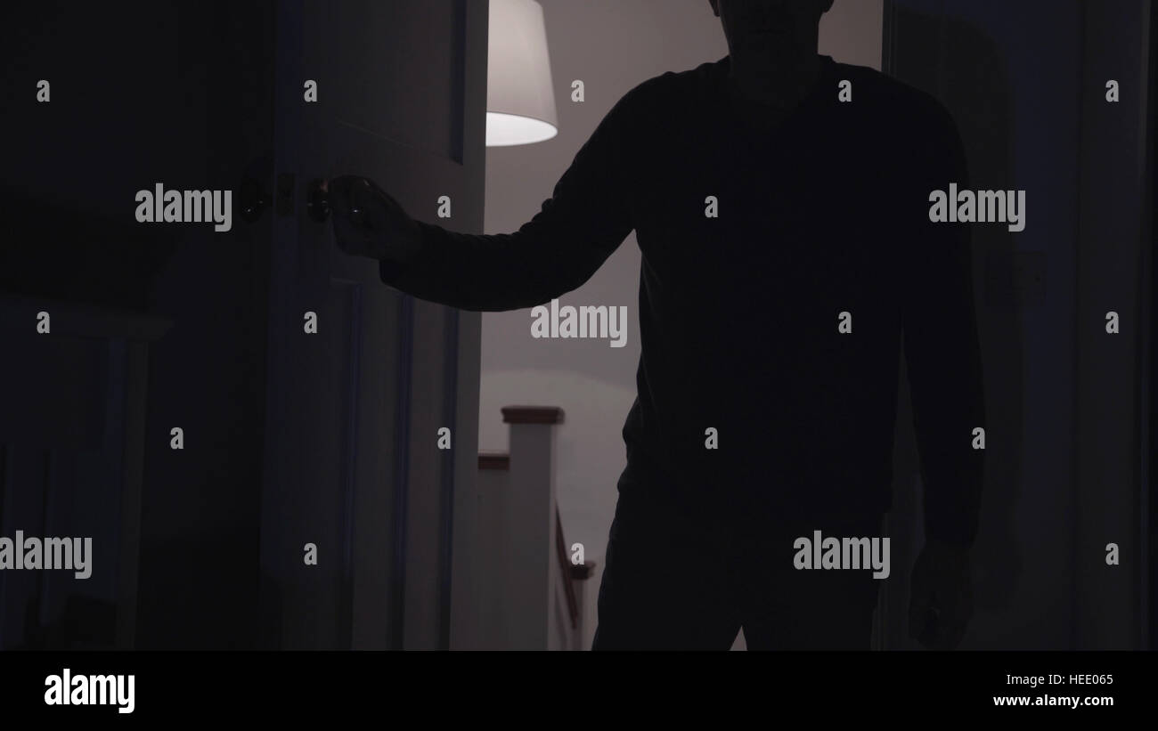 Silhouette of a man opening a door to a dark room. Stock Photo