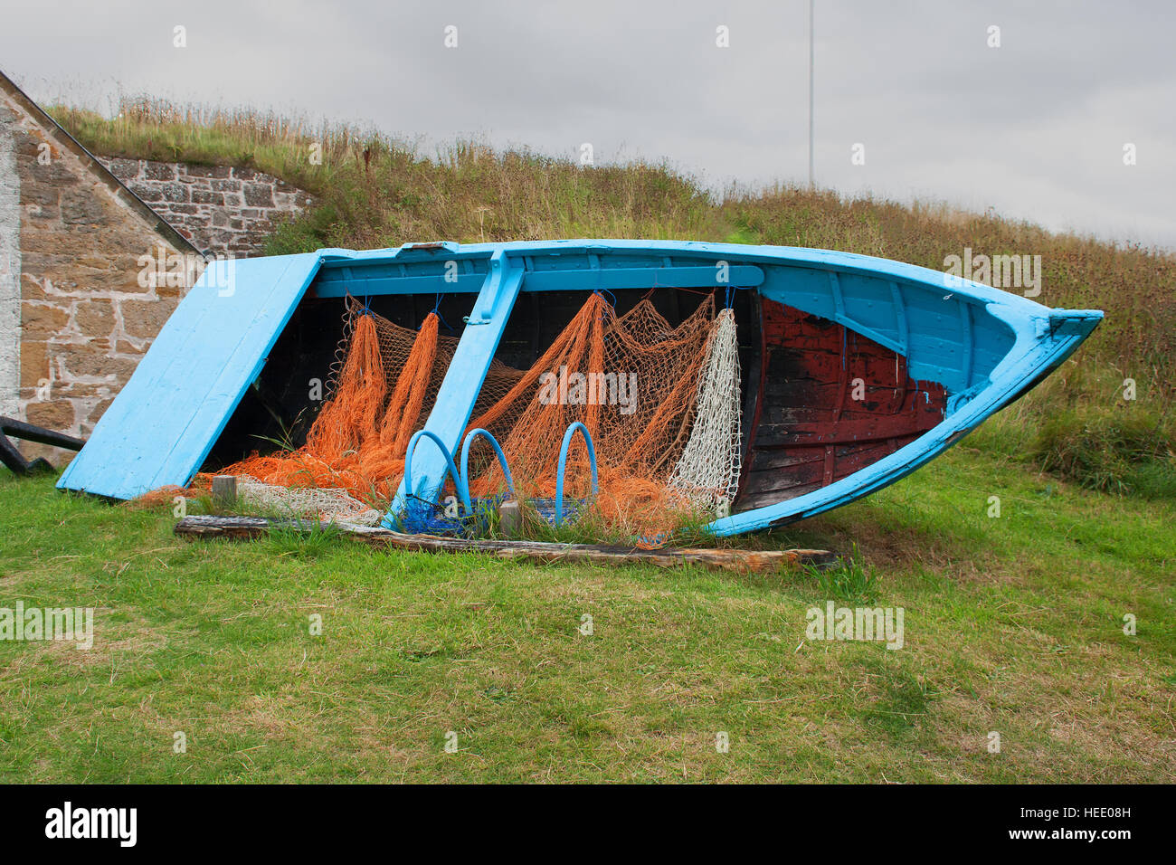 Small open fishing boat with nets and lobster pot preserved for posterity outside a small