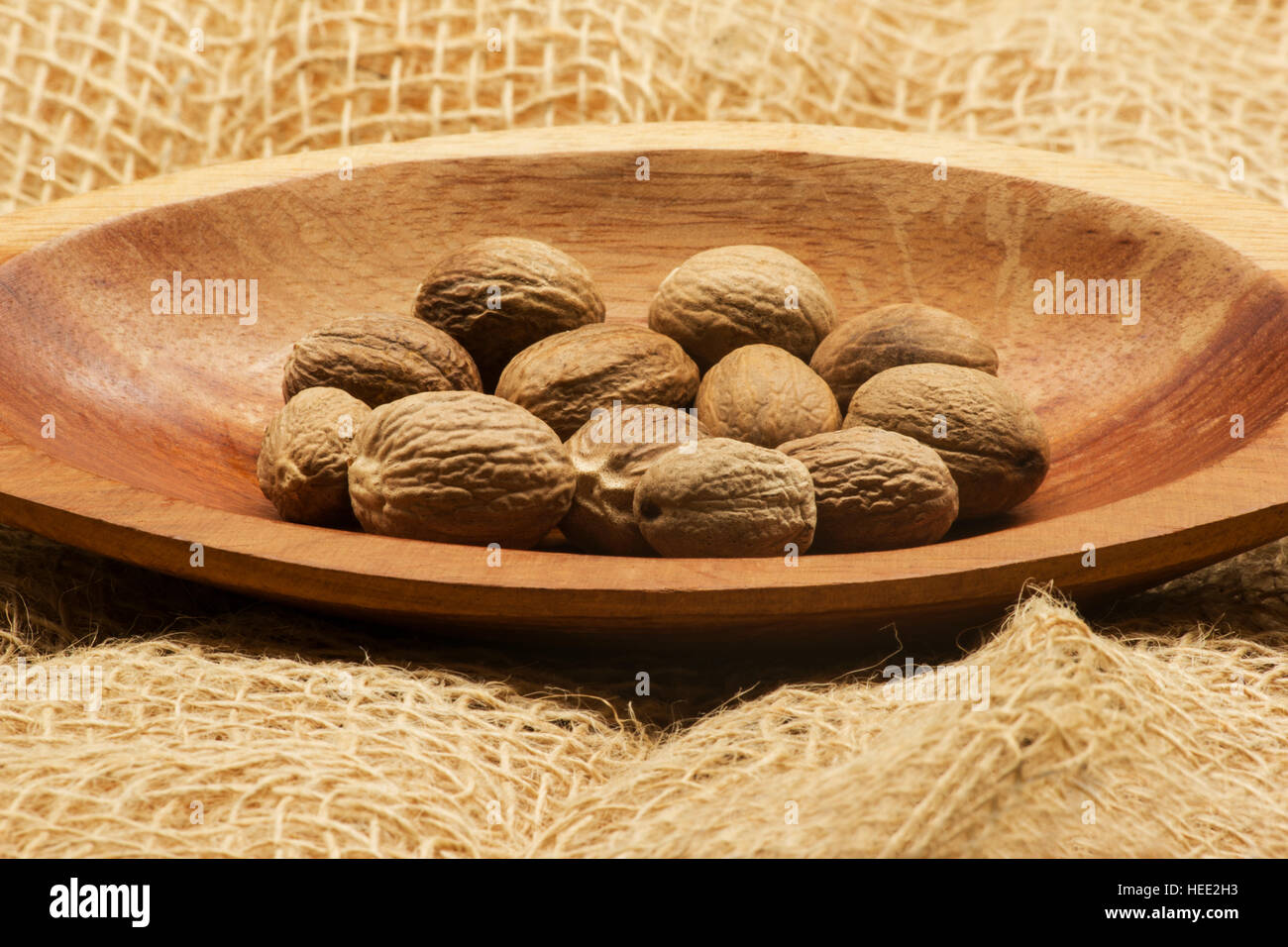 Nutmegs (Myristica fragrans) in a wooden bowl on burlap Stock Photo