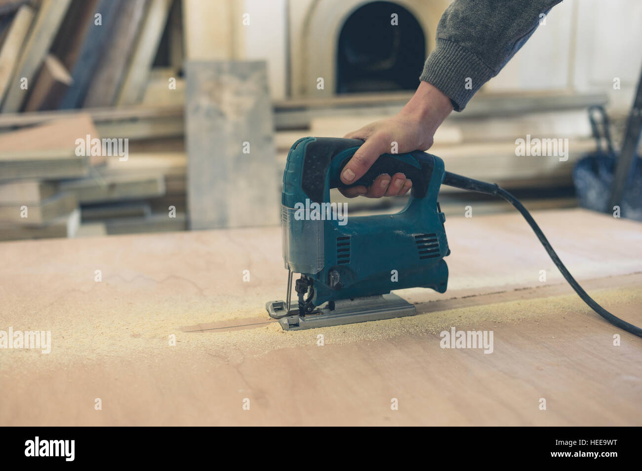 A young worker is cutting a sheet of plywood with a jigsaw indoors Stock Photo