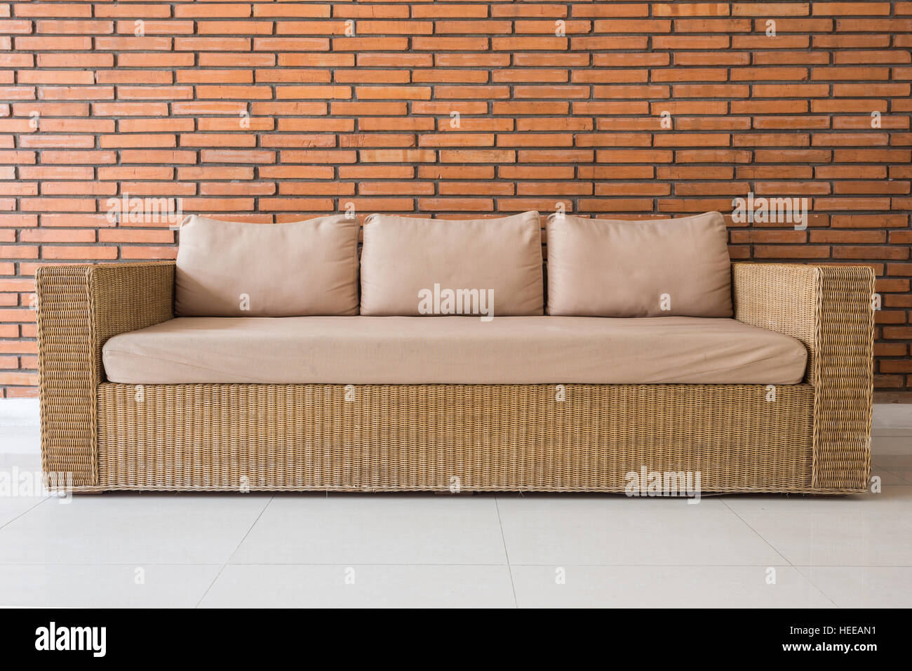 https://c8.alamy.com/comp/HEEAN1/rattan-sofa-with-grey-cushions-and-red-brick-wall-background-HEEAN1.jpg