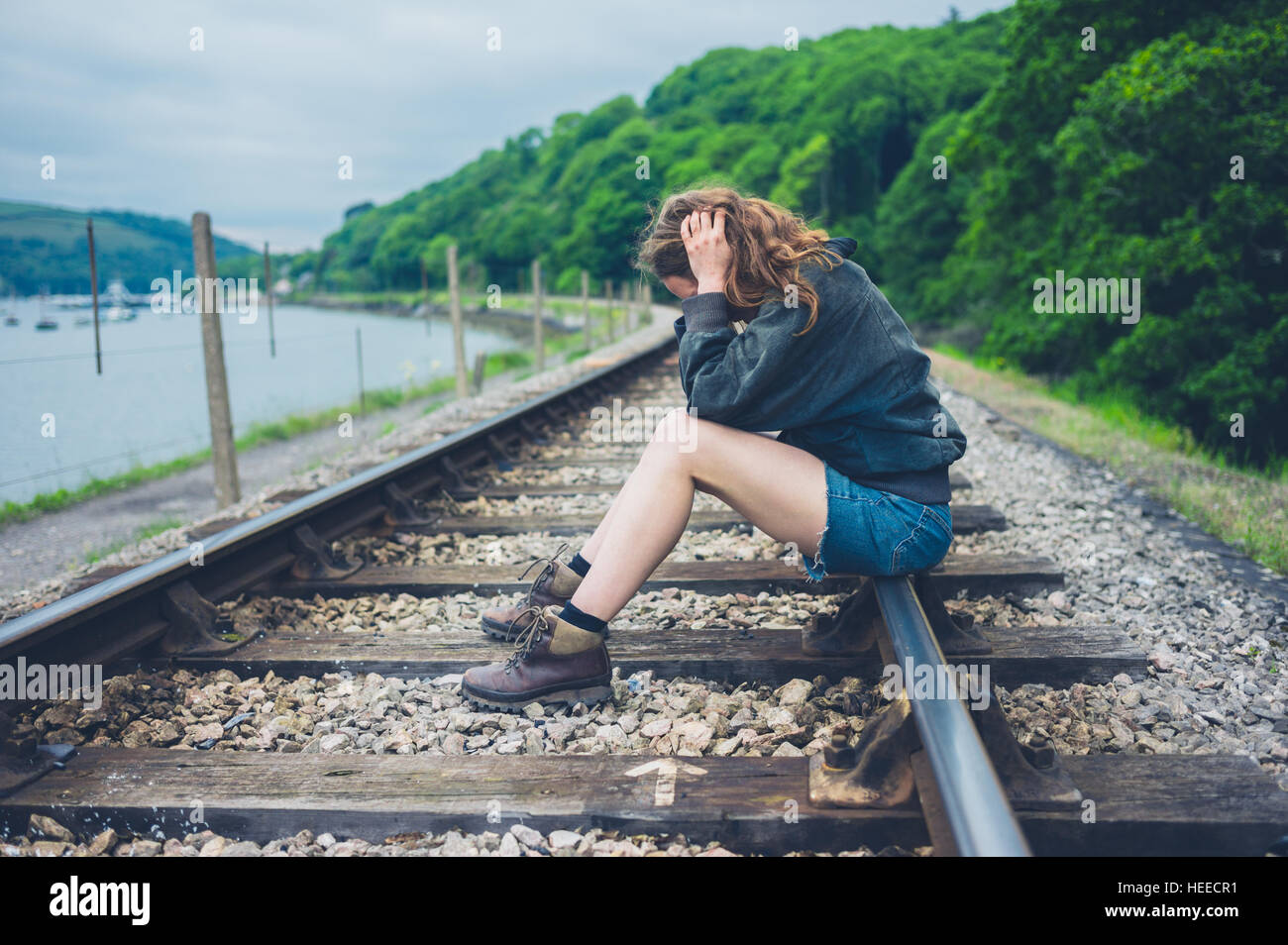 A sad young woman is sitting on the railroad tracks Stock Photo Alamy