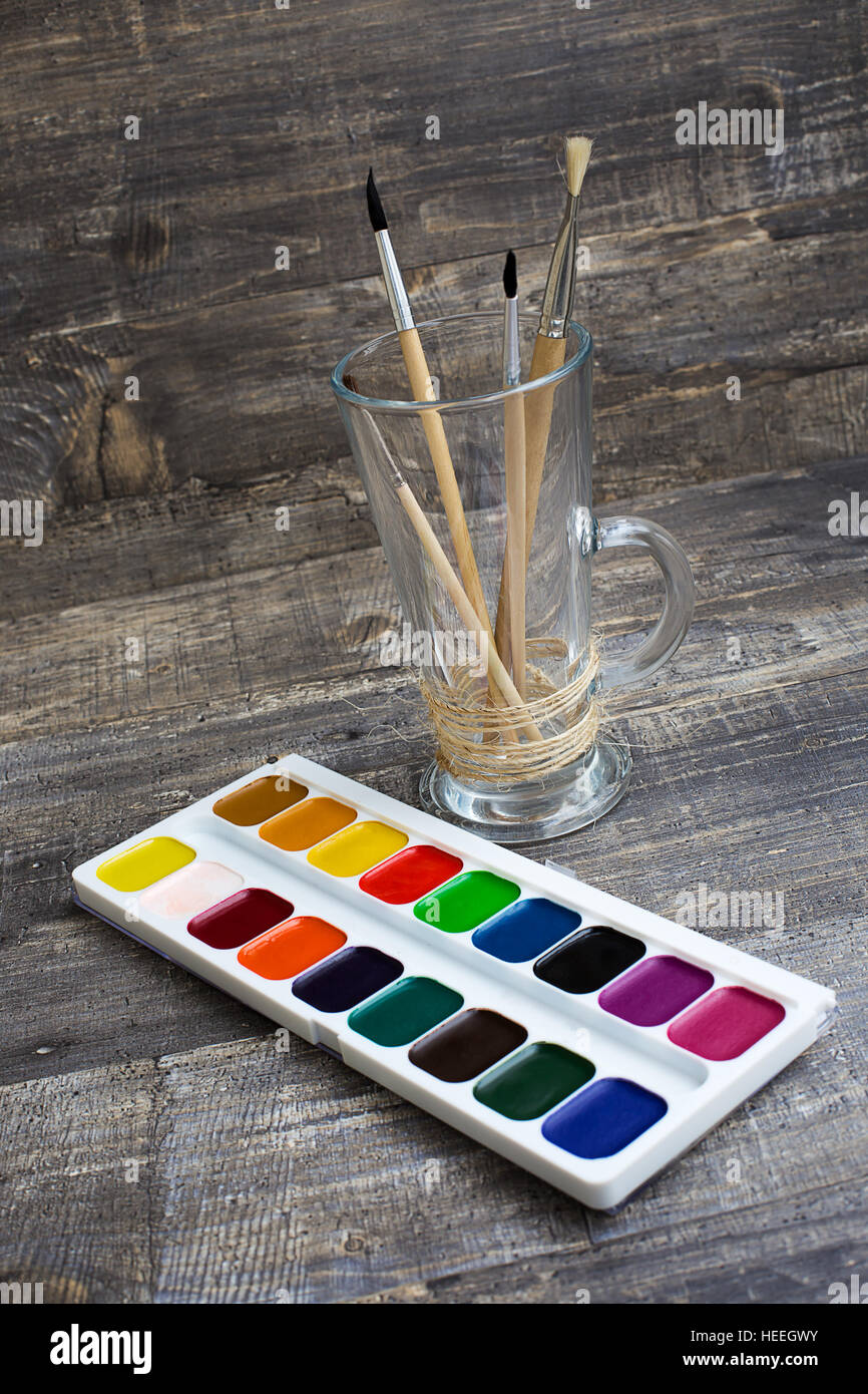 Brushes in vase and watercolor paints on wooden background. Vertical diagonal imagination Stock Photo