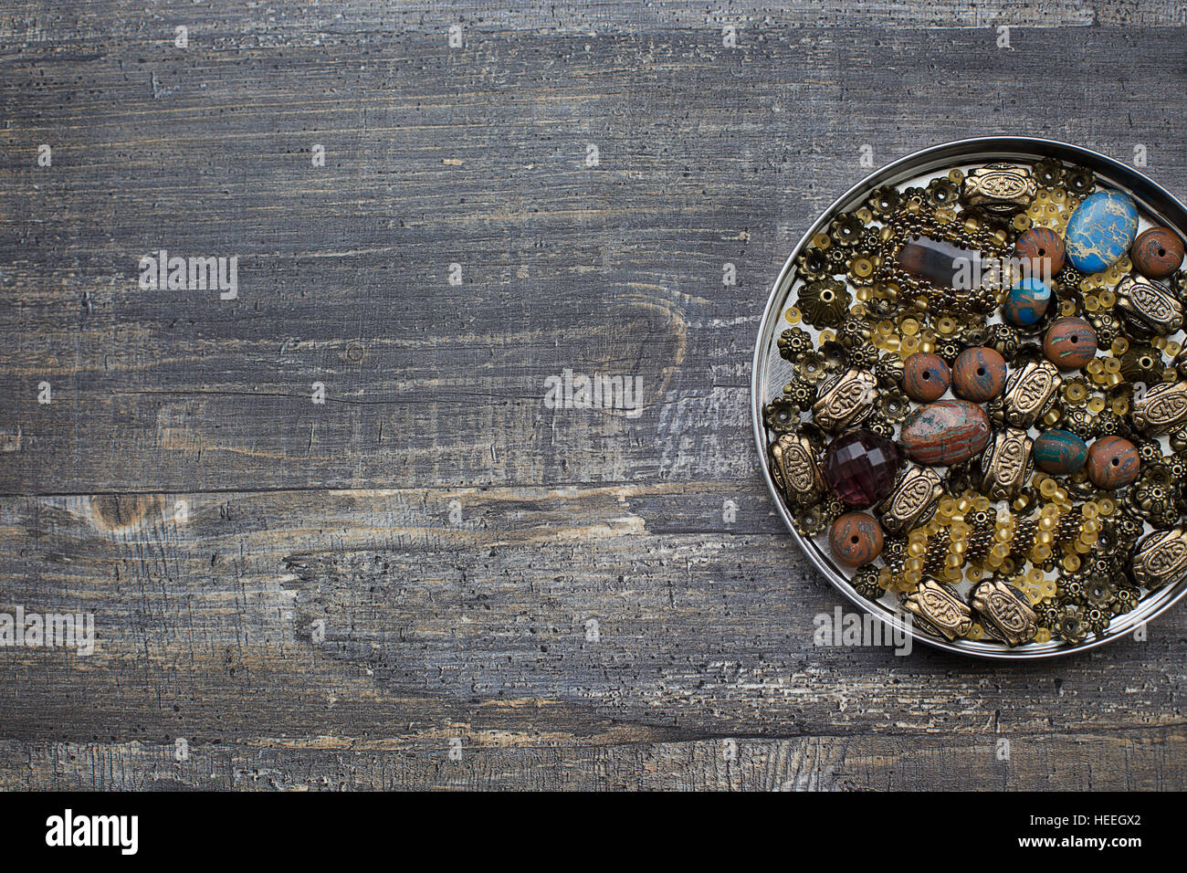 Different small beads into tin lid on wooden background Stock Photo