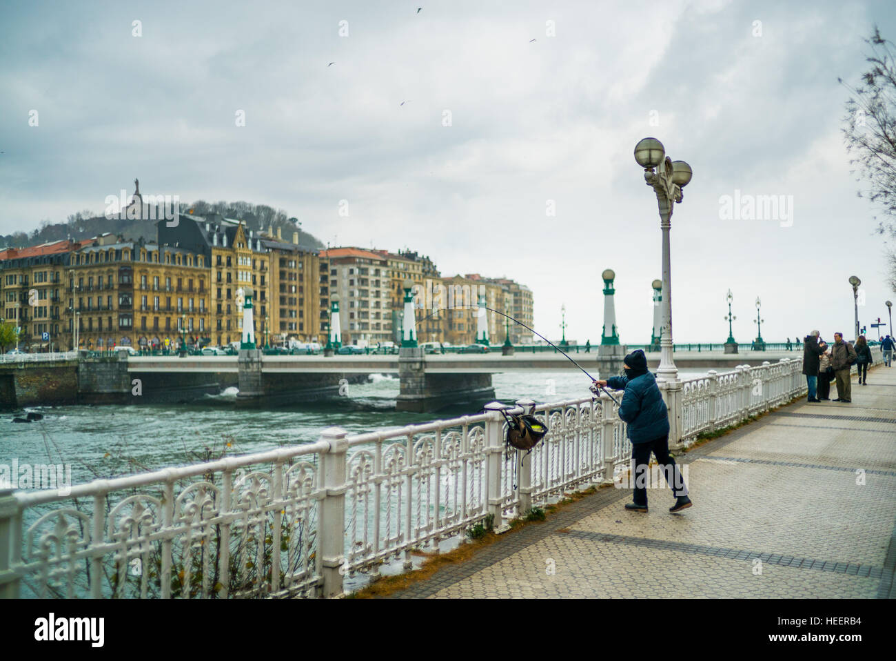A woman fishes from the boardwalk on a cold winters day in San Sebastian Stock Photo