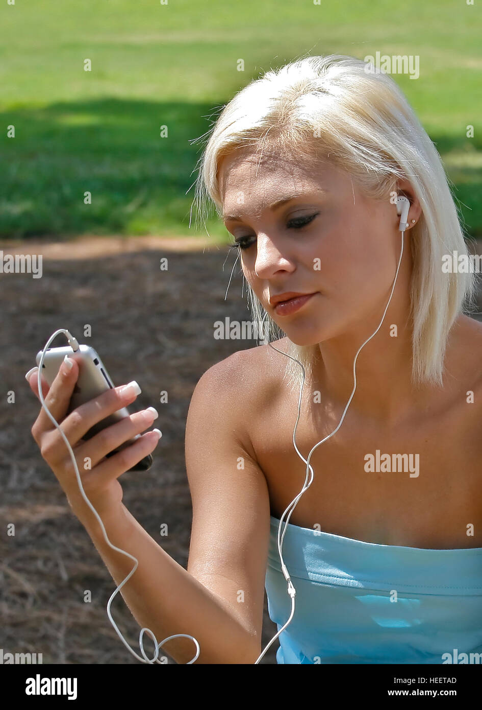 Blond woman using portable music player with headphones outdoors in park. Stock Photo