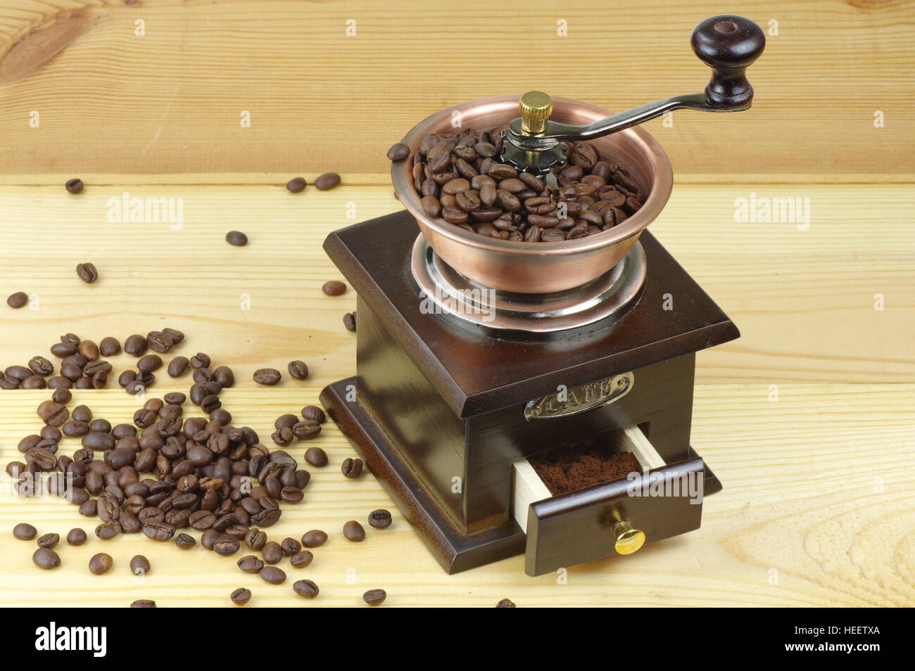 Old-style manual coffee grinder on a rustic table with wooden planks. Around the mill are scattered coffee beans. Stock Photo