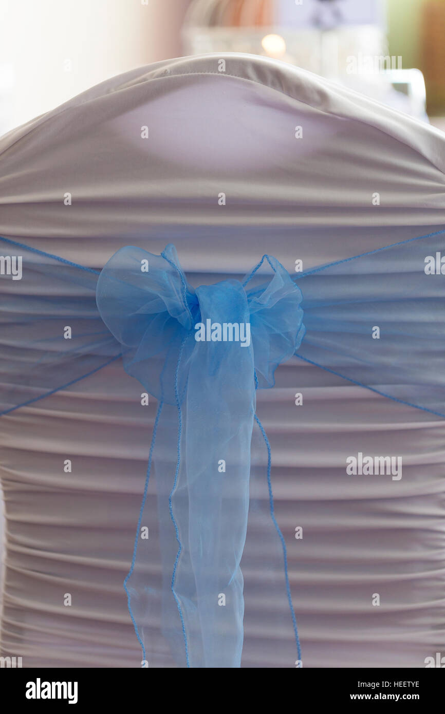 Chair covered in white ruched fabric with baby blue organza sash tied in a bow at wedding celebration dinner Stock Photo