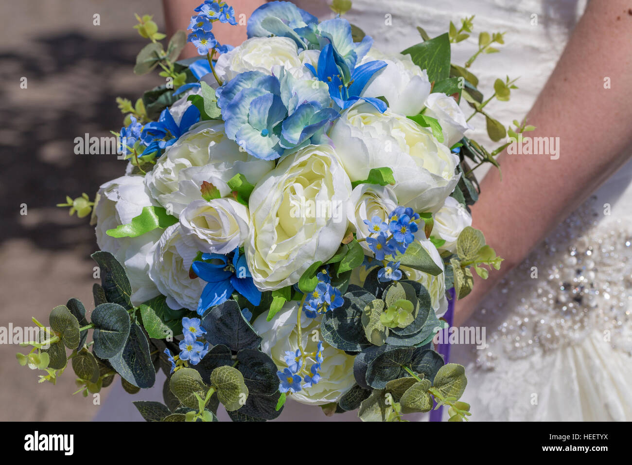 Blue and white bridal bouquet held by bride against traditional white jeweled wedding dress with pearls Stock Photo