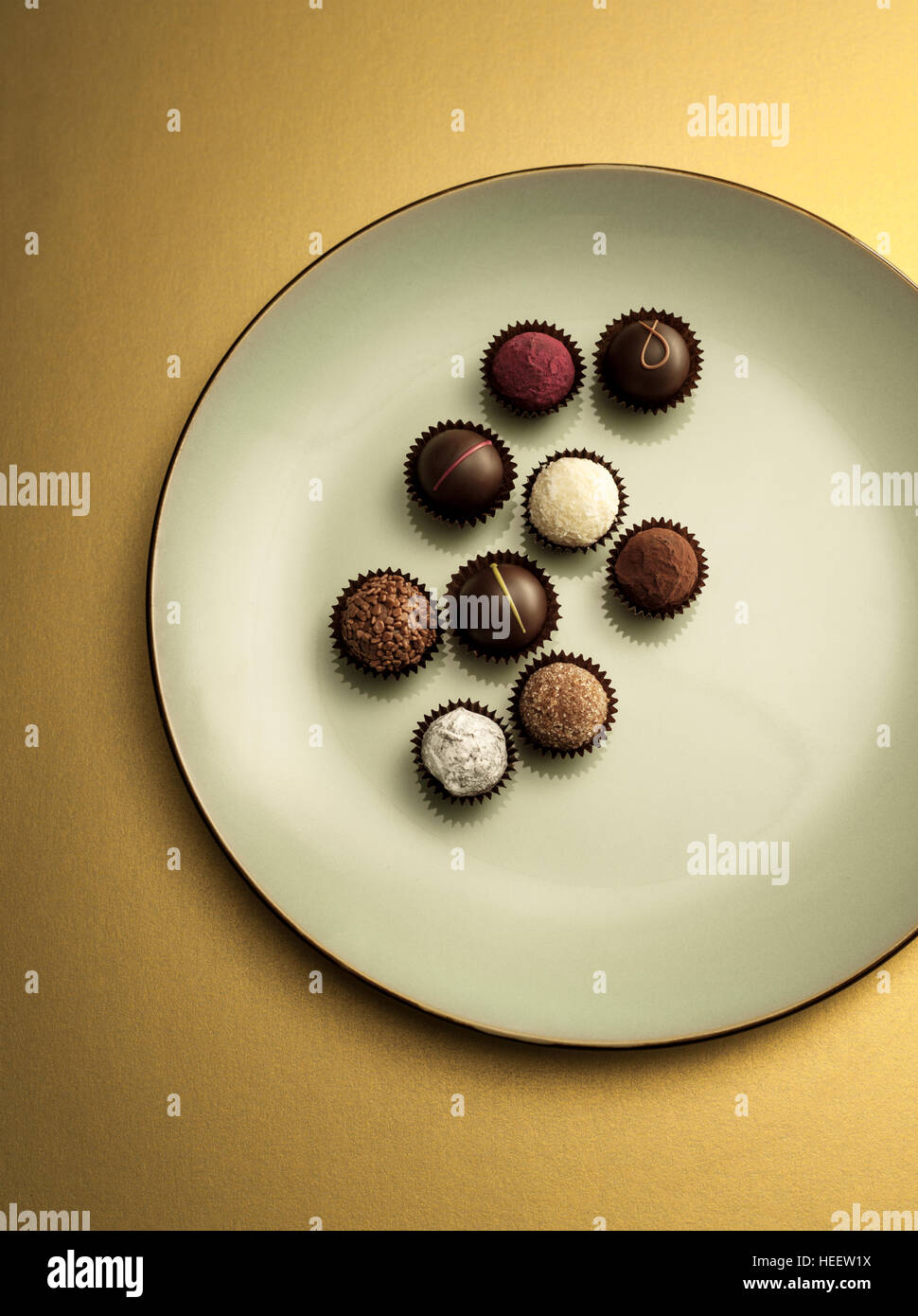 Chocolate pralines and truffles on green plate and gold background