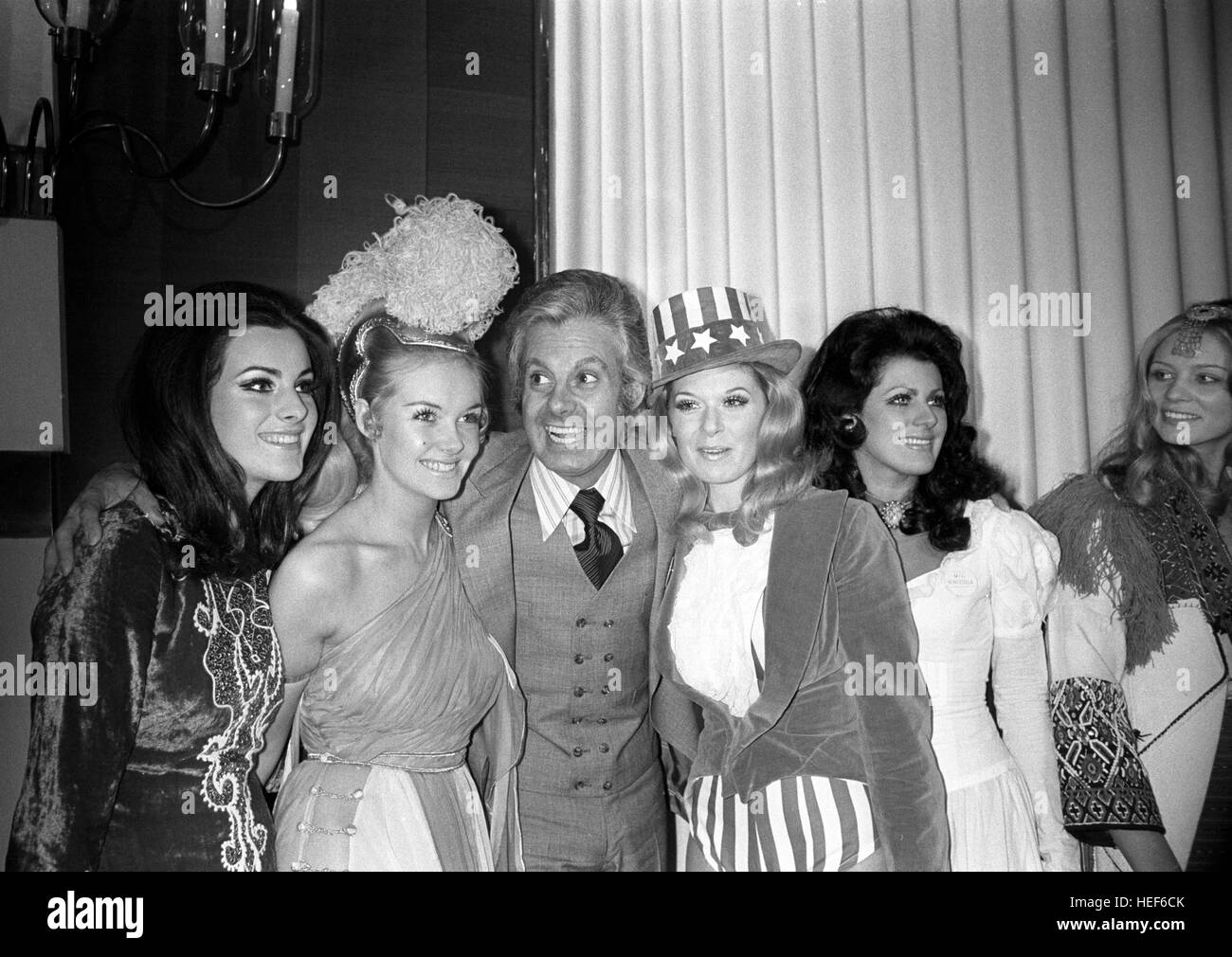 Female impersonator, Danny La Rue, shed his drag image to meet the contestants of the Miss World 1970 contest in London. Mr La Rue (centre) poses with the Miss World contestants (l-r) Afet Tugbay (Miss Turkey), Yvonne Anne Ormes (Miss UK), Sandra Anne Wolsfeld (Miss USA) and Tomasa Nina de las Casas Mata (Miss Venezuela). The meeting took place at the Variety Club of Great Britain Savoy Hotel Luncheon, in honour of the contestants who wore national dress for the occasion. Stock Photo