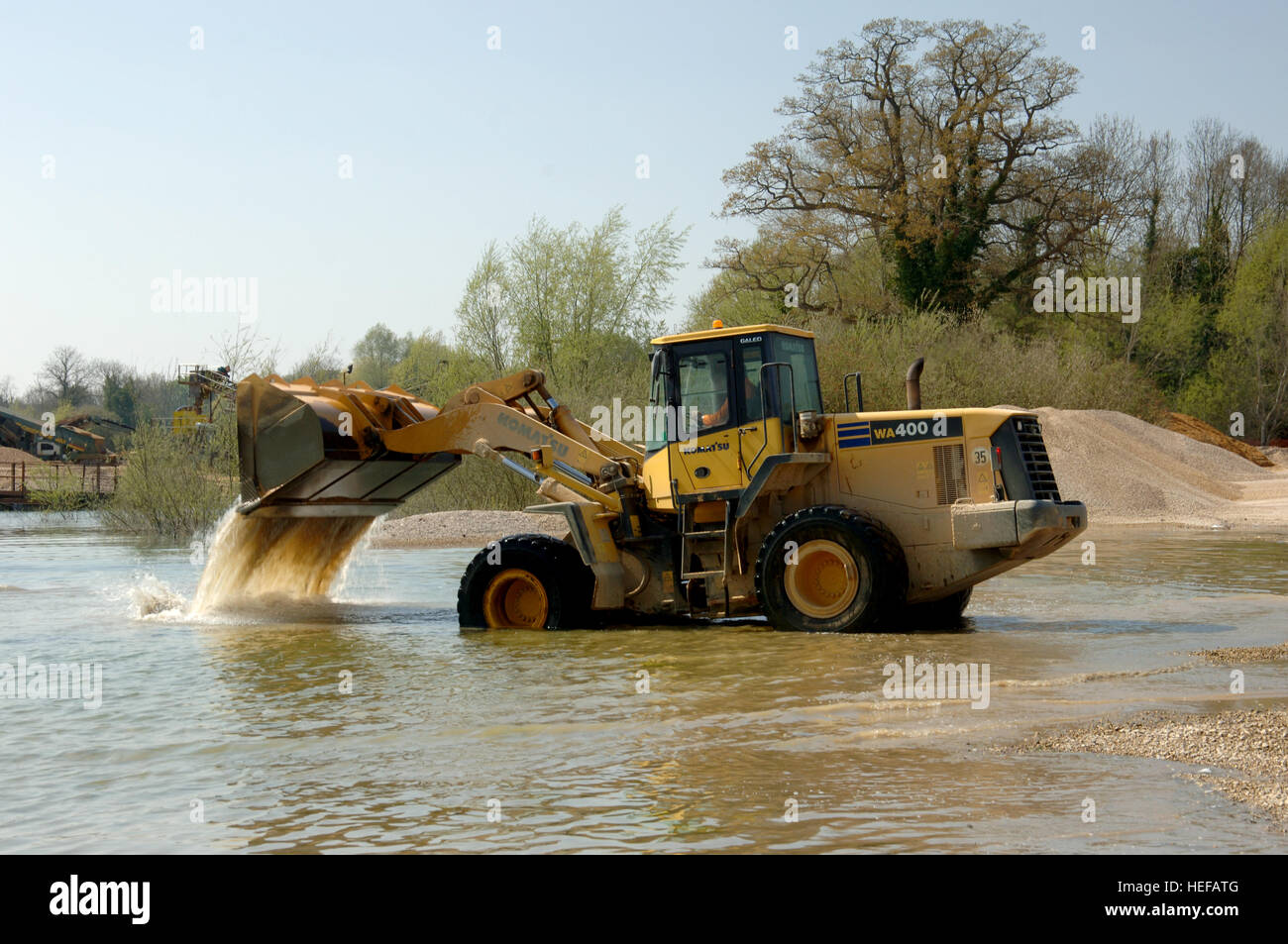 Large front loader digger working in a quarry lake, dumping tons of