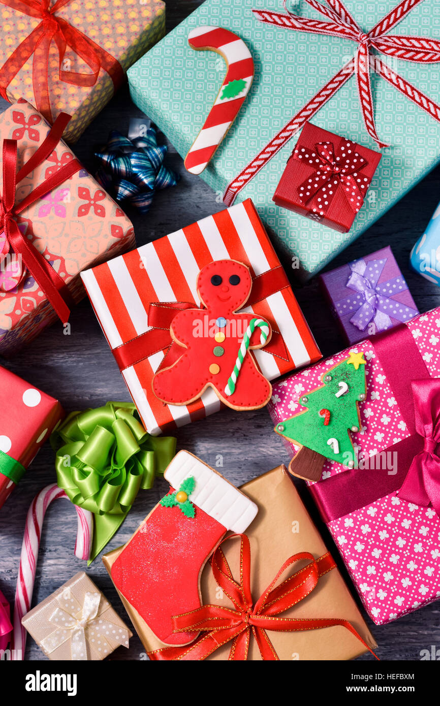 high-angle shot of some christmas biscuits and a pile of gifts wrapped in nice papers and tied with ribbons of different colors on a rustic wooden sur Stock Photo