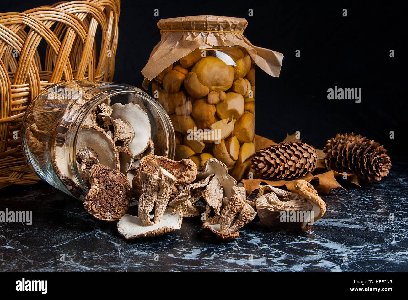 Two glass jars with wild mushrooms on black marble background. One jar