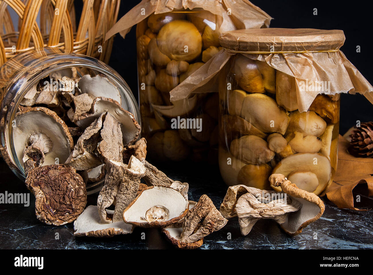 Two glass jars with wild mushrooms on black marble background. One jar