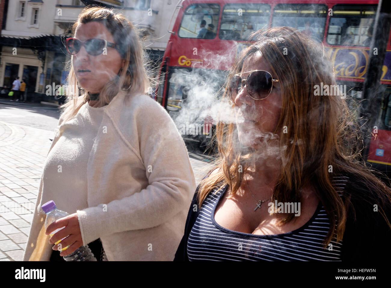 A female wearing aviator sunglasses exhales cigarette smoke on a bright and sunny London afternoon Stock Photo