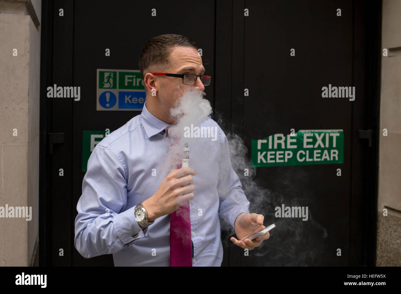 A businessman enjoying an E-Cigarette on the street Stock Photo