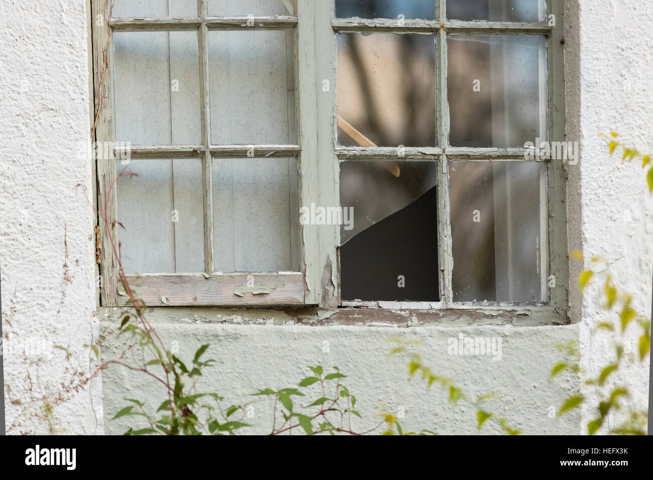 old cottage window with broken window pane and flaking paint Stock Photo