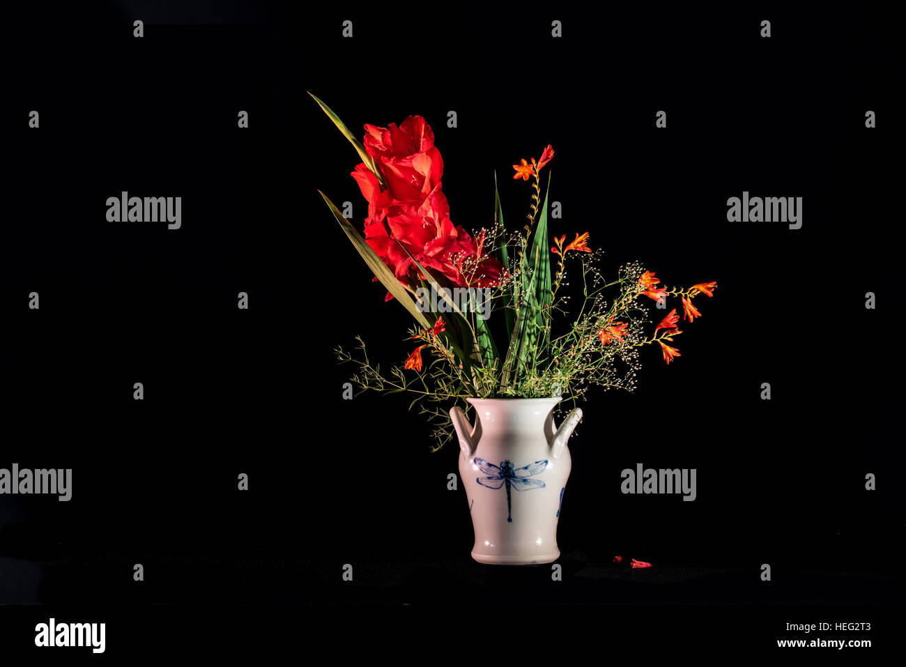 A lovely bouquet in red with gladiolus, montbretia 'Lucifer'  and baby's breath in a dragonfly pottery on a black background Stock Photo