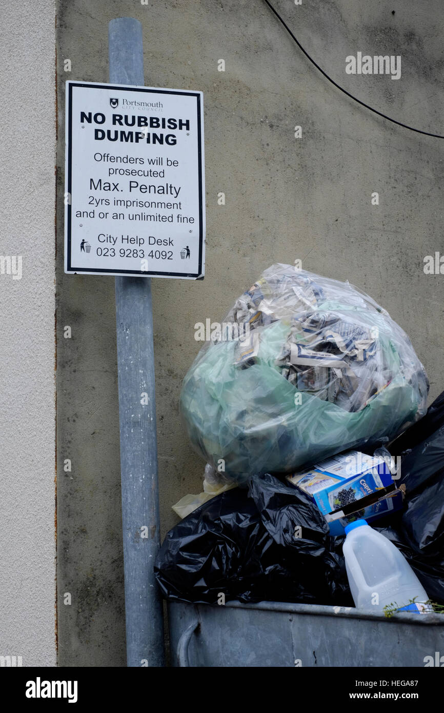 a garbage filled skip next to a sign saying no rubbish dumping england uk Stock Photo