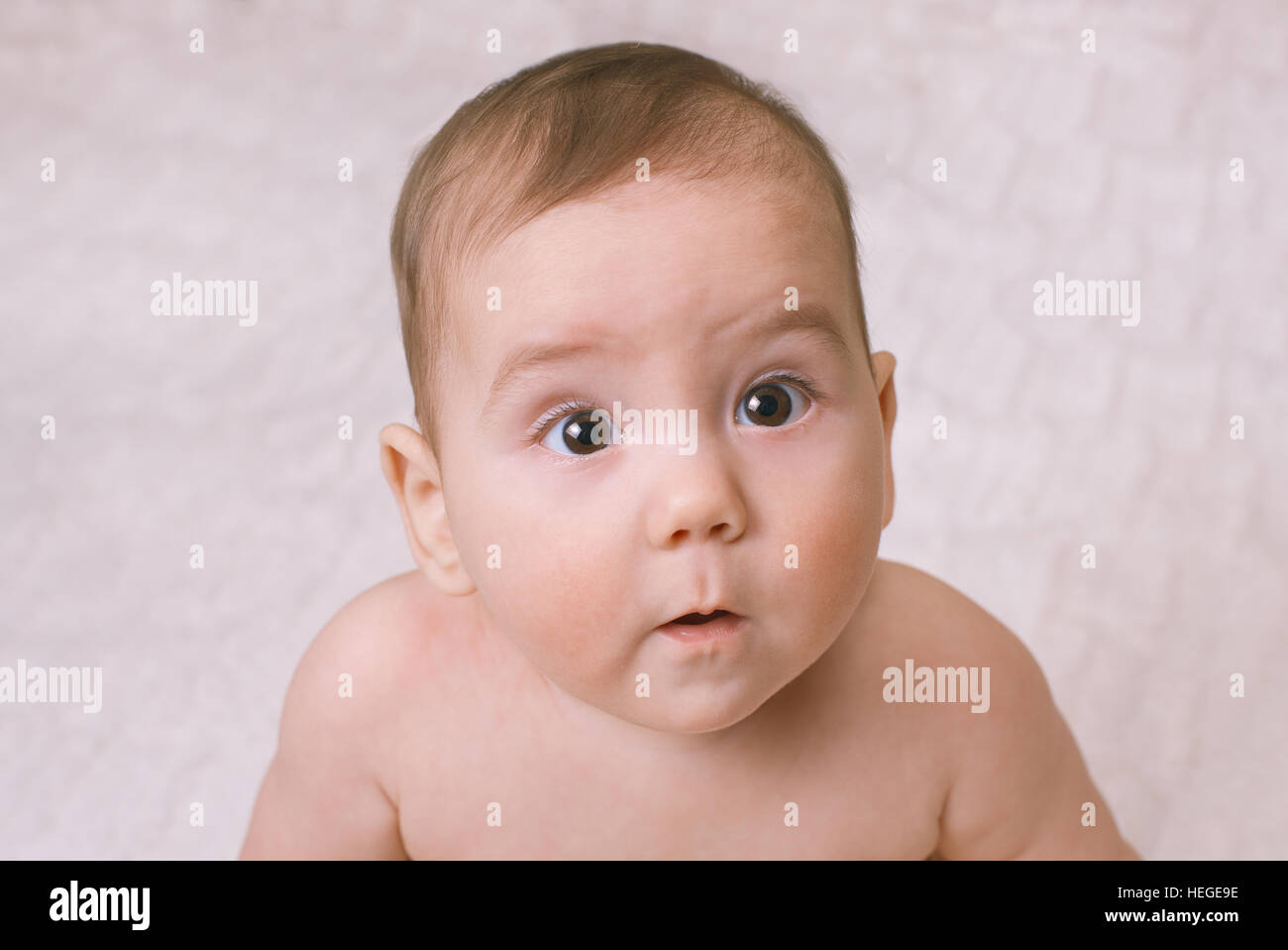 Wide eyed curious little baby staring up to the side of the camera with a mesmerised look , close up high angle Stock Photo