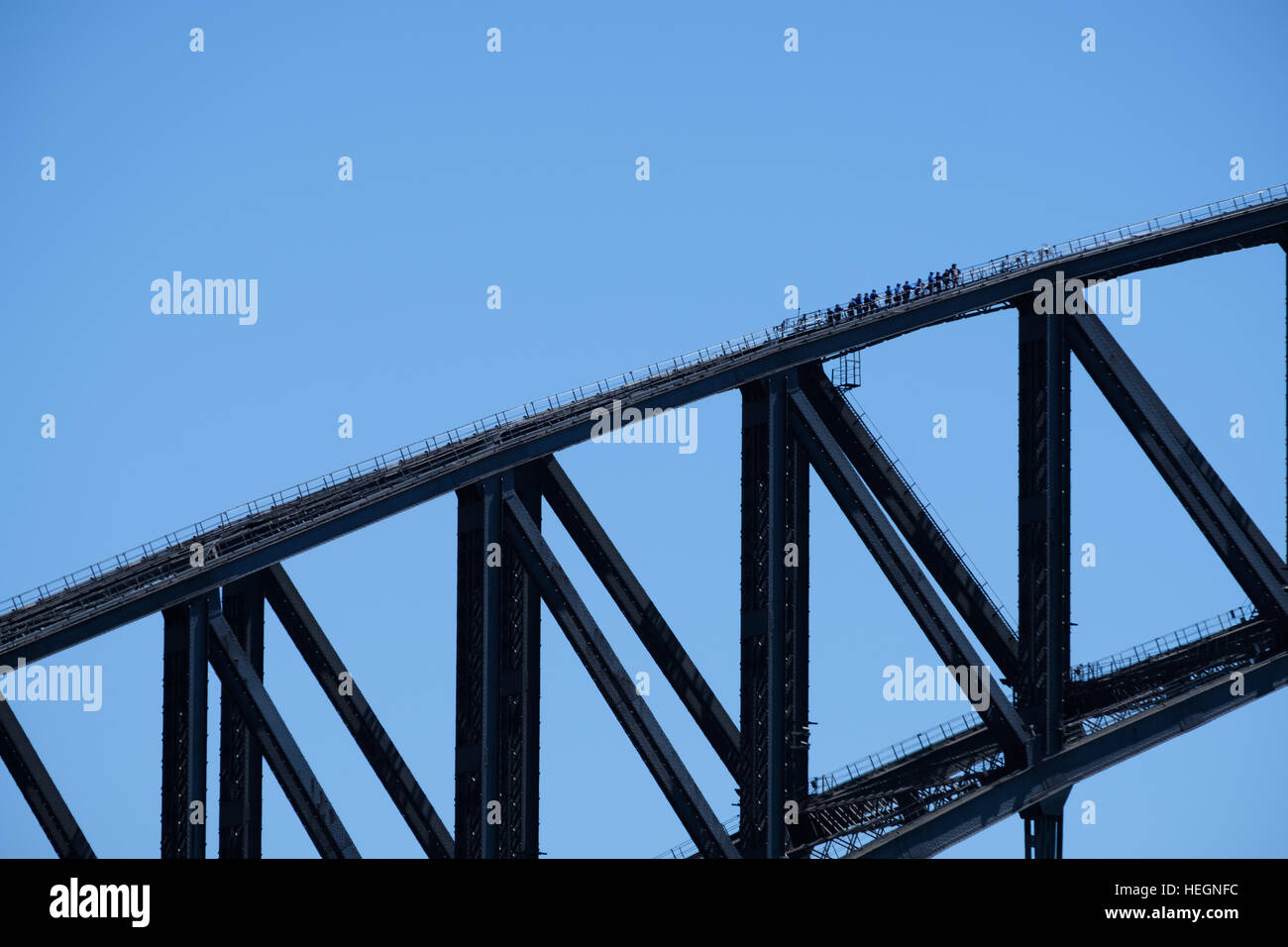 Group of people walking over Sydney harbour bridge against blue sky Stock Photo