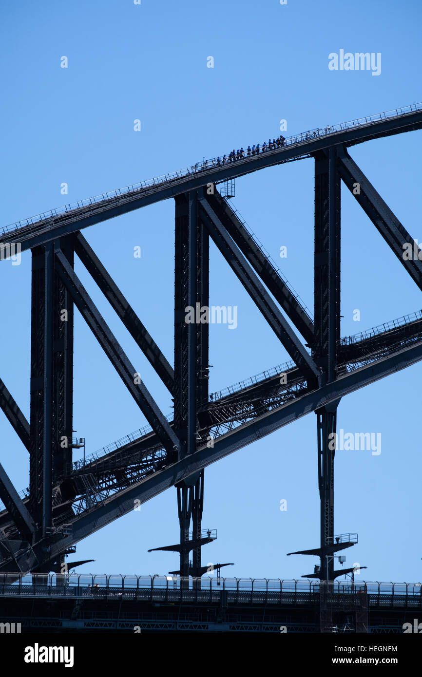 Group of people walking over Sydney harbour bridge against blue sky Stock Photo